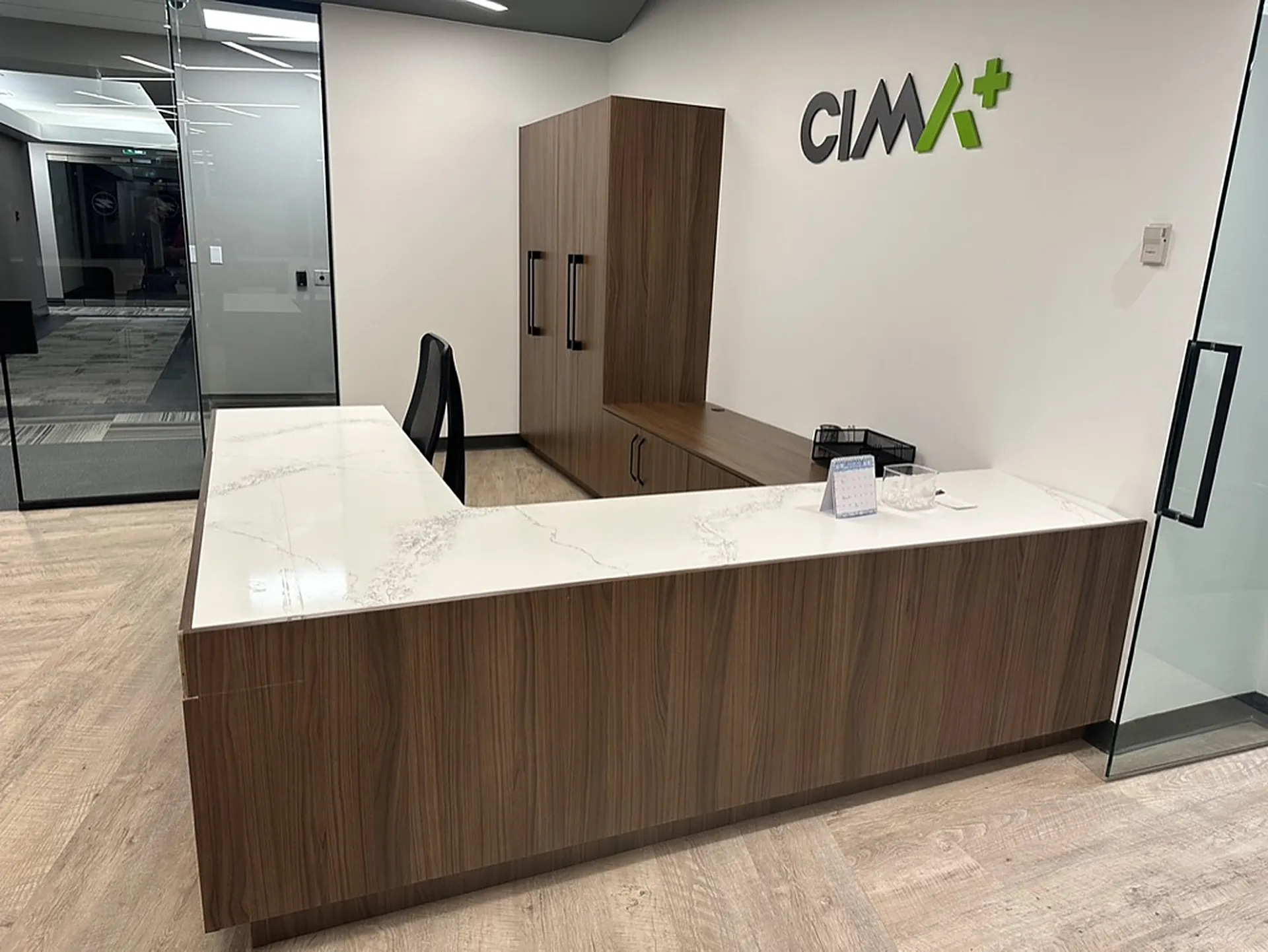 Wood and quartz reception desk with CIMA+ wall signage